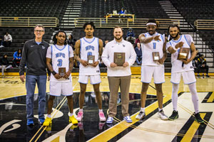 People mid basketball court holding plaques.