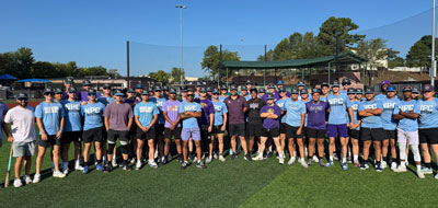 Baseball team standing on field in blue and purple shirts.