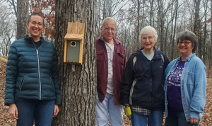 People standing around a tree with a bird box attached to it.