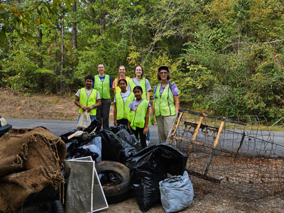 People in green vest standing behind collected trash in bags.