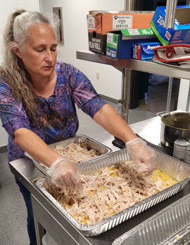 Person shredding chicken in an aluminum pan.