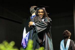 Two people in graduation robes hugging.