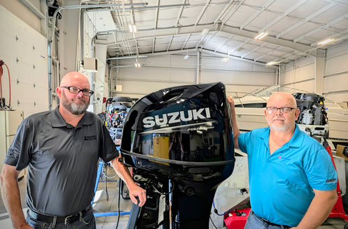 Two people standing next to a black Suzuki boat motor.