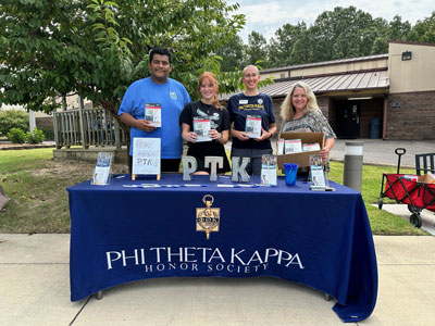 Four people standing behind a table holding scientific calculators. Tablecloth says Phi Theta Kappa Honor Society.