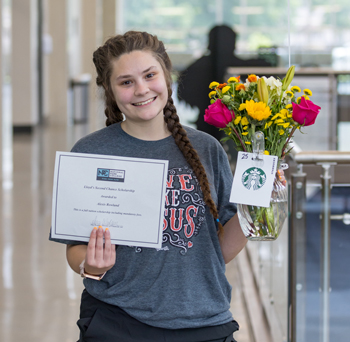 Person posing for a picture with a certificate and bouqet of flowers with a starbucks gift card.
