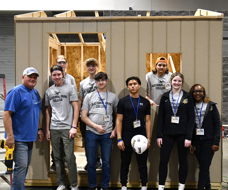 Construction Technology students and their teacher standing in front of a shed they are building.