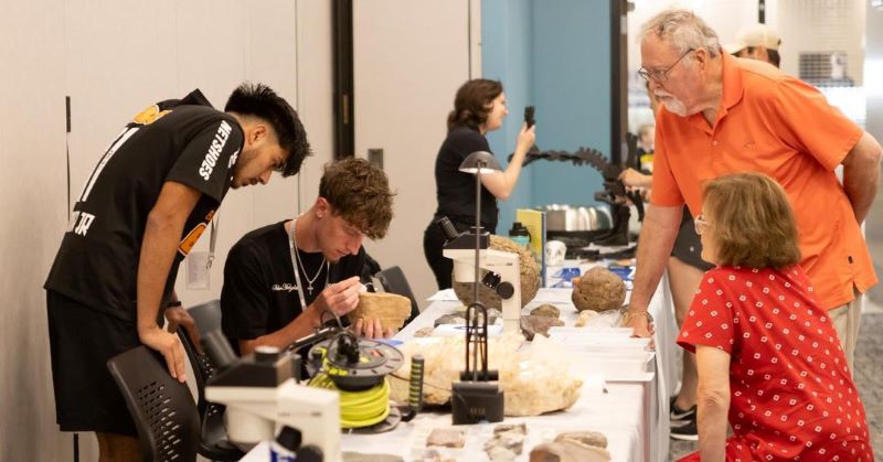 people gather around table looking at rocks, fossils, etc. 