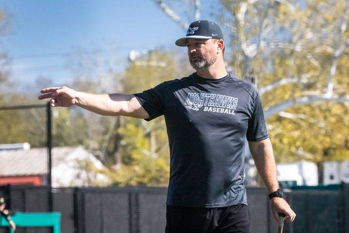 Coach Rich Thompson giving handsignals to baseball players.