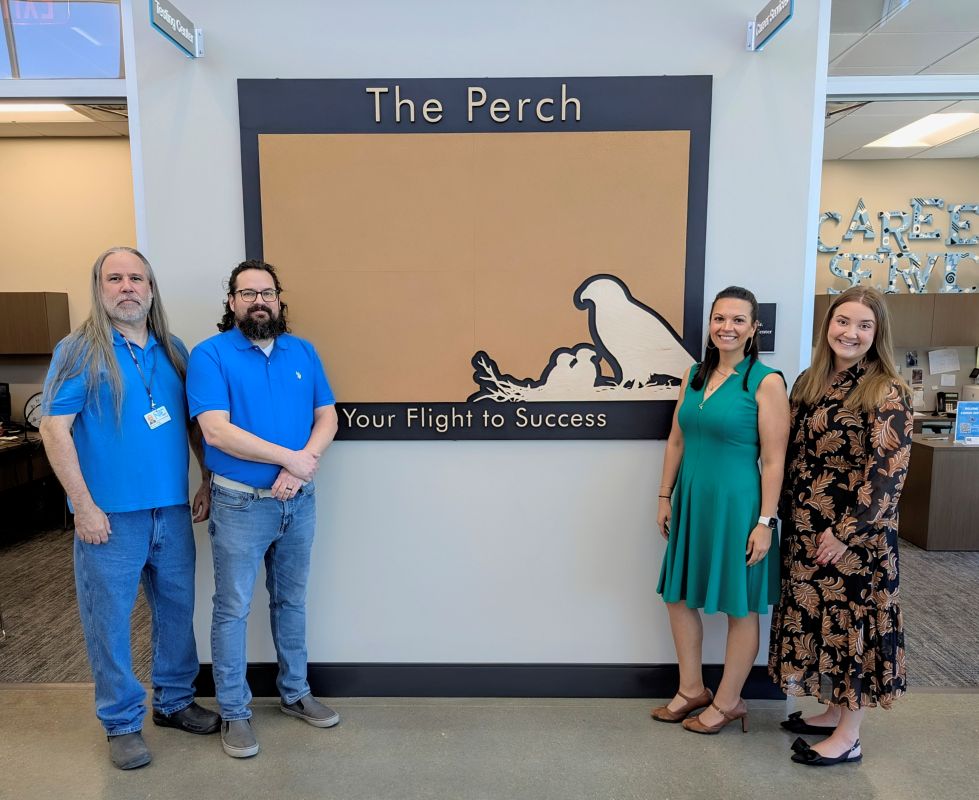Four people standing to the sides of a bulletin board.
