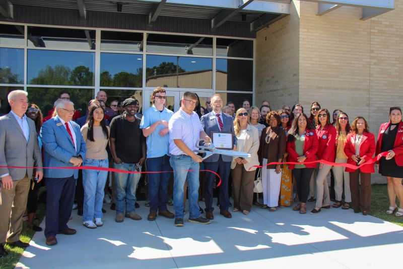 A group of people cutting a red ribbon in front of a building.