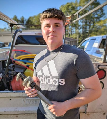 Caleb Roberts standing at the end of a truck bed holding a wrench.