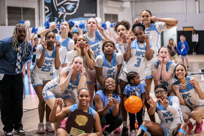 Women's basketball team each holding a piece of the cut net from the winning game.