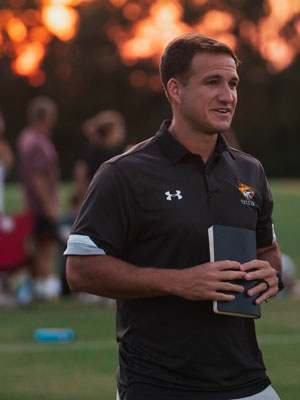 Grant Gartner, assistant soccer coach on field holding bottled drink.