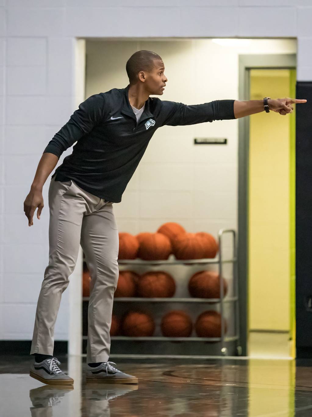 Coach Dominique Battles on basketball court pointing with left hand.