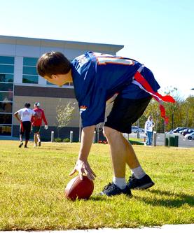 Student reaching down for football in a game of flag football.